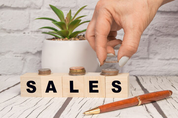 Sales written on wooden cubes, business concept. Hands place a stacked increasing coin on a wooden block, office background