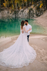 Newlyweds are standing near a beautiful lake. Middle Eastern groom and Caucasian bride embrace on the beach.