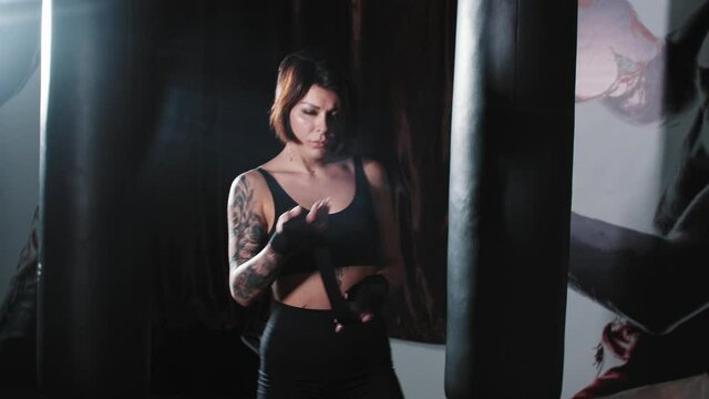 Tattooed woman boxer binding her hands and stands in the fighting pose