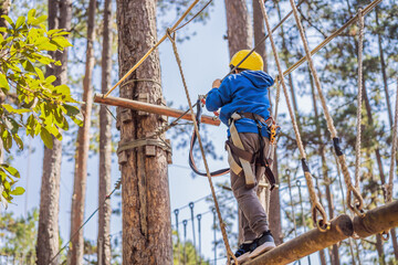 Happy child in a helmet, healthy teenager school boy enjoying activity in a climbing adventure park on a summer day
