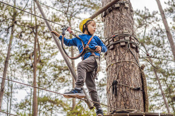 Happy child in a helmet, healthy teenager school boy enjoying activity in a climbing adventure park on a summer day