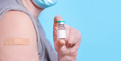 Man with a bottle of vaccine and a plaster on his shoulder after getting Covid-19 vaccine on a blue background. Medicine concept, vaccination, coronavirus immunity, safe travel. Baner. Copy space