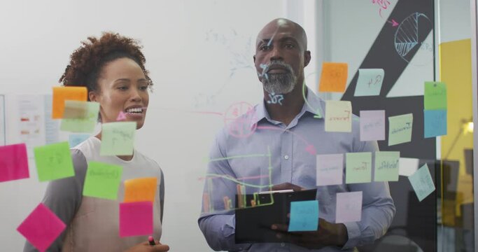 Diverse businessman and businesswoman brainstorming and smiling by transparent board with memo notes
