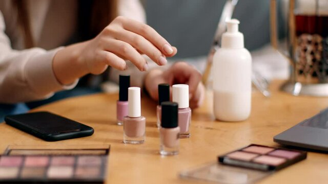 Female hands choosing nail polish on table, woman preferring nute color, making manicure at home, close up, slow motion