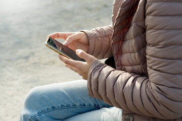 A woman with a mobile phone in hand in a warm jacket on the street.