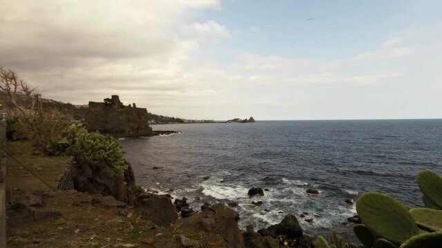 Time Lapse di un panorama siciliano costiero con le onde del mare che si infrangono sugli scogli e il castello di Aci Castello e i Faraglioni di Aci Trezza sullo sfondo