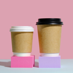 Paper coffee containers with lid on trendy minimal coloured background. Coffee to go container mockup. Two containers for hot drinks on colourful podiums.