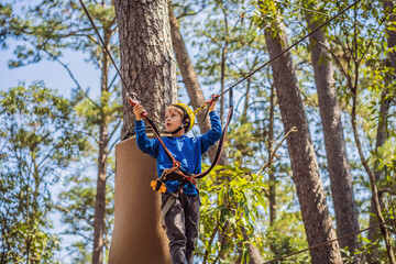 Happy child in a helmet, healthy teenager school boy enjoying activity in a climbing adventure park on a summer day