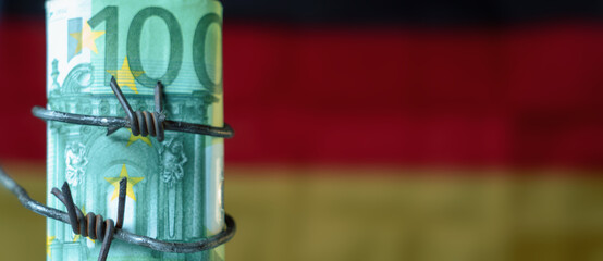 One hundred EURO bancnotes wrapped in barbed wire against flag of Germany as symbol of global economic crisis and recession. Copy space for design.