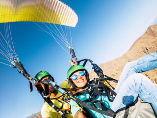 Active young adult people woman enjoy paraglide activity fliying in the sky with professional pilote in the back - cheerful happy female people fly and have fun with paragliding - obrazy, fototapety, plakaty