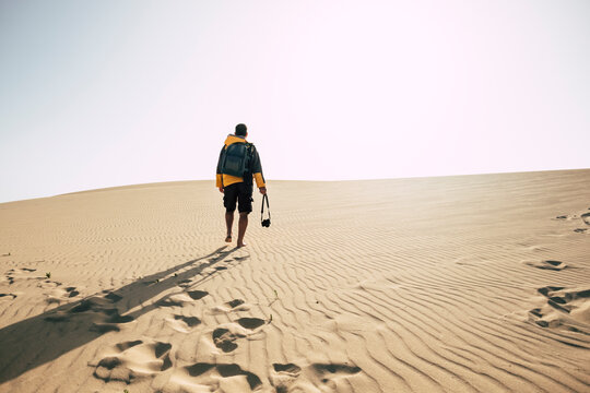 Man walking alone on desert sand dunes - explore and adventure outdoor leisure activity - camera and backpack equipment to enjoy exploration and wild landscape arid place