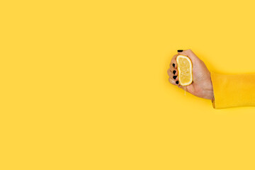 Mano de mujer sosteniendo y exprimiendo medio limón sobre un fondo amarillo liso y aislado. Vista de frente. Copy space