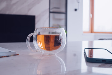 Glass cup of tea next to cup and mobile phone on the table at home