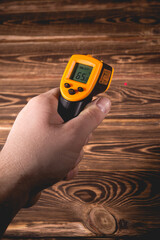 A man holds a yellow-black pyrometer on a wooden background. A device for non-contact temperature...