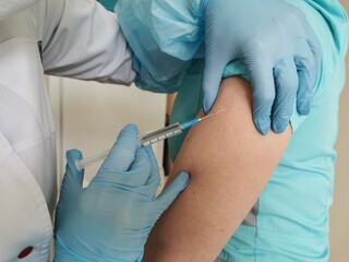 Fototapeta premium A healthcare professional gives an injection into the shoulder. Vaccination against coronavirus, influenza.