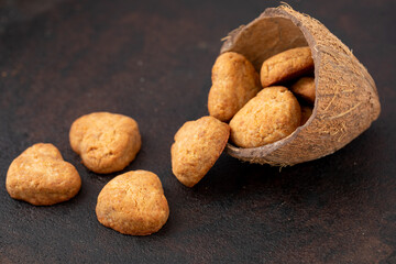 Homemade coconut biscuits from coconut paste, heart crumbly coconut cookies in half coconut shell on black stone board. Horizontal