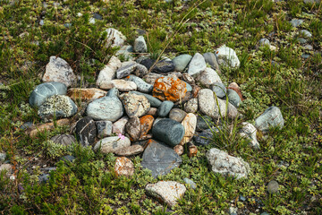 Pile of stones with lichen and moss on green grass. Art nature background with many stones on ground. Altai pagan cemetery. Ancient pagan burial place of Altaians. Pagan rite on Altai. Heap of stones.