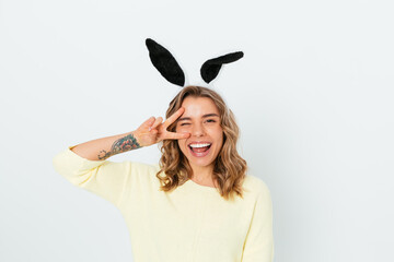 Joyful young woman wearing bunny ears shows peace gesture