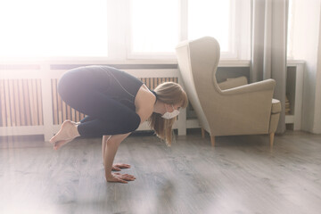 Meditating woman wearing a medical face mask to protect from corona virus, yoga position on mat home
