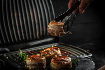Medallions steaks from the beef tenderloin covered bacon on grill with smoke dark background....