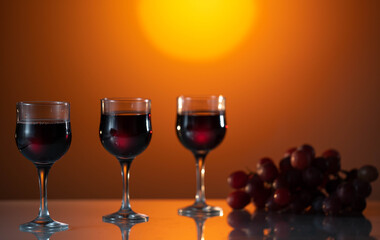 Tree glasses of wine on a beautiful sunset background. holiday mood. Reflected surface. Grape is near the glasses