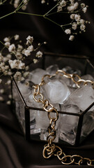 gold necklace in box with ice and gypsophila on dark brown atlas background