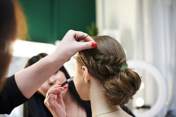Fototapeta premium Getting ready for party. Young pretty girl sitting in beauty salon while hairdresser and make-up artist making her look beautiful. Professional work process in studio. Love yourself. Bride's morning.