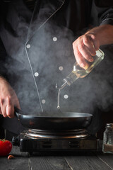 The chef adds olive oil to pan while cooking. Working environment on the restaurant kitchen table....