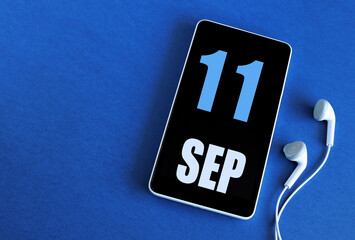 September 11. 11 st day of the month, calendar date. Smartphone and white headphones on a blue background. Place for your text. Autumn month, day of the year concept