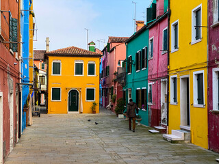 Fototapeta na wymiar Unrecognizable person walking in the typical and very colorful streets of Burano. We see laundry being dried outside