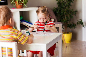 Little girl and boy children at home sit at the table and draw with markers, happy childhood