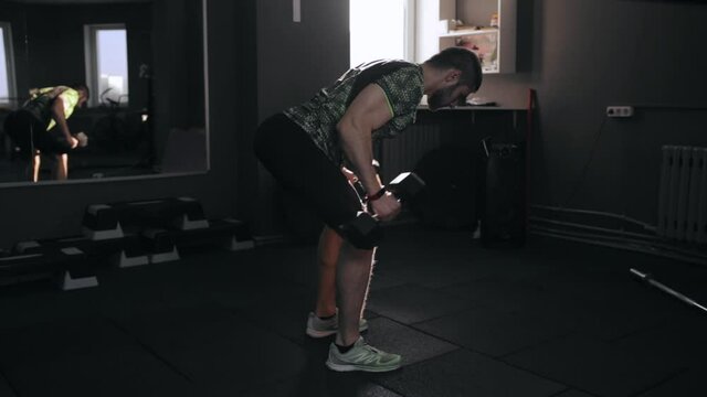Side view of muscular enduring male athlete doing triceps kickbacks with dumbbells during intense workout in gym 