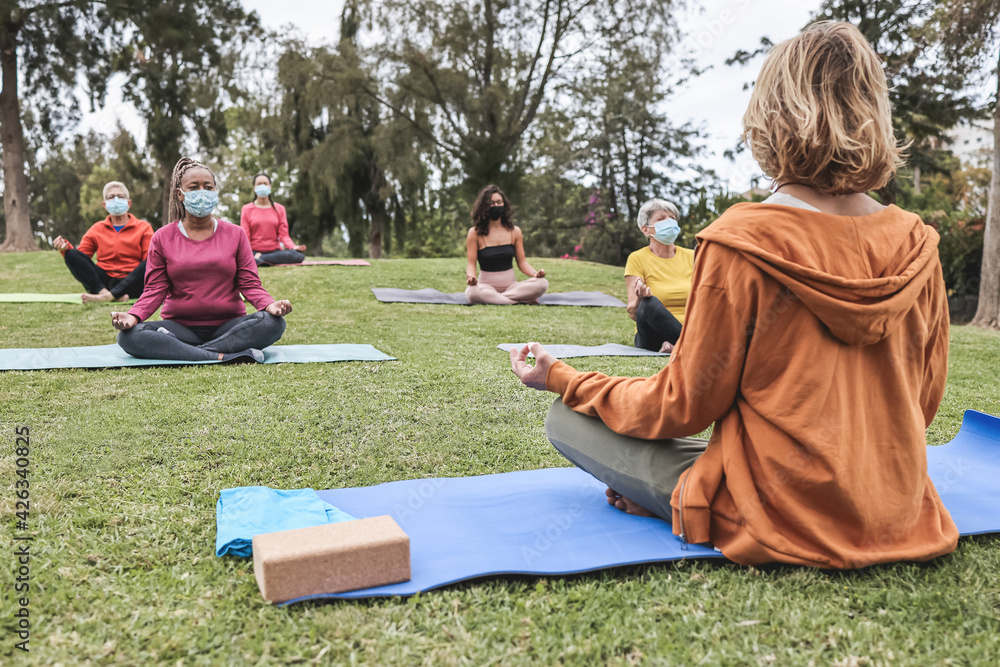 Wall mural People doing yoga class while wearing safety masks at city park - Focus on teacher back