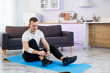 A young man goes in for sports at home, ties the laces on sneakers before training. Healthy lifestyle