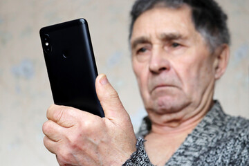Elderly man with mobile phone looking on smartphone display. Concept of online communication in retirement, sms, social media and news