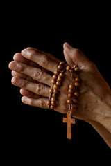 Praying hands of Indian Catholic woman with wooden rosary isolated on a black background.