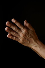 Praying hands of an old Indian Catholic woman isolated on a plain black background.