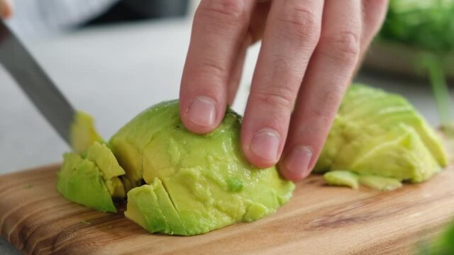 Male hands cutting ripe avocado on a wooden board, closeup view