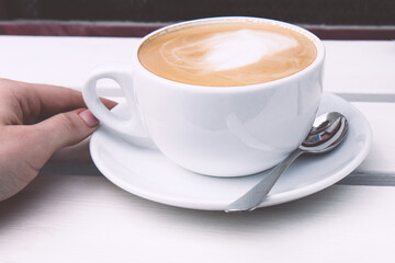 Cappuccino in a white ceramic cup on a white wooden bench. Open-air rustic morning coffee