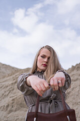 Beauty portrait of a young blond girl in a vintage dress. She is posing on a sandy landscape.