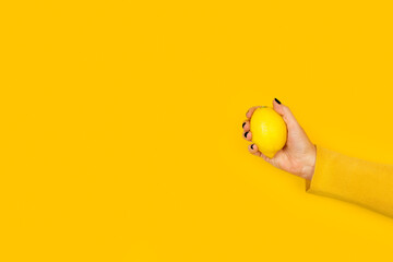Mano de mujer sosteniendo un limón sobre un fondo amarillo brillante liso y aislado. Vista de...