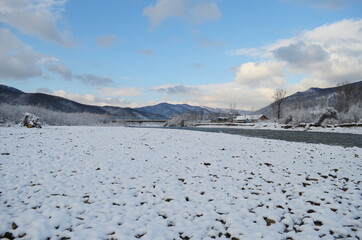 A frozen river in a wintry landscape. Winter landscape with forest, cloudy sky and sun.