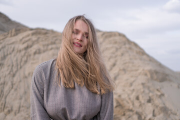 Beauty portrait of a young blond girl in a vintage dress. She is posing on a sandy landscape.