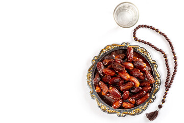 Vintage bowl of dates with a glass of water. Dates in a bowl and islamic prayer beads. Date palm fruits or kurma, ramadan on white background. Ramadan kareem with dates. Top view with free space