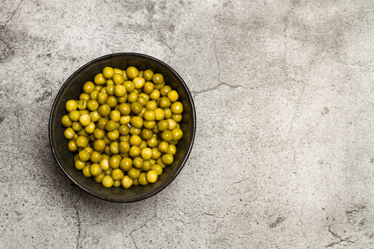 Guisantes naturales y frescas en un cuenco negro sobre un fondo r&uacute;stico gris . Vista superior. Copy space