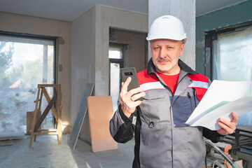 The foreman informs the customer about the progress of repair work. Engineer with drawings and phone in a building under construction. Monitoring the progress of construction.
