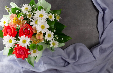 Greeting card. Bouquet of flowers and folds of blue fabric on a dark background