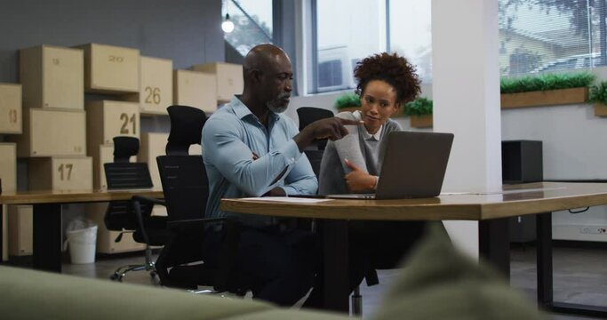 Diverse male and female business colleagues talking and using laptop in office