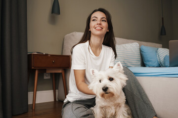 Happy young woman playing with her dog in bedroom