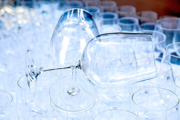 Two red wine crystal glasses lay on a raw of other grasses prepared for big party. Blurred. Catering and restaurant utensils. wedding organisation. Wine tasting. Background picture. Group of objects 